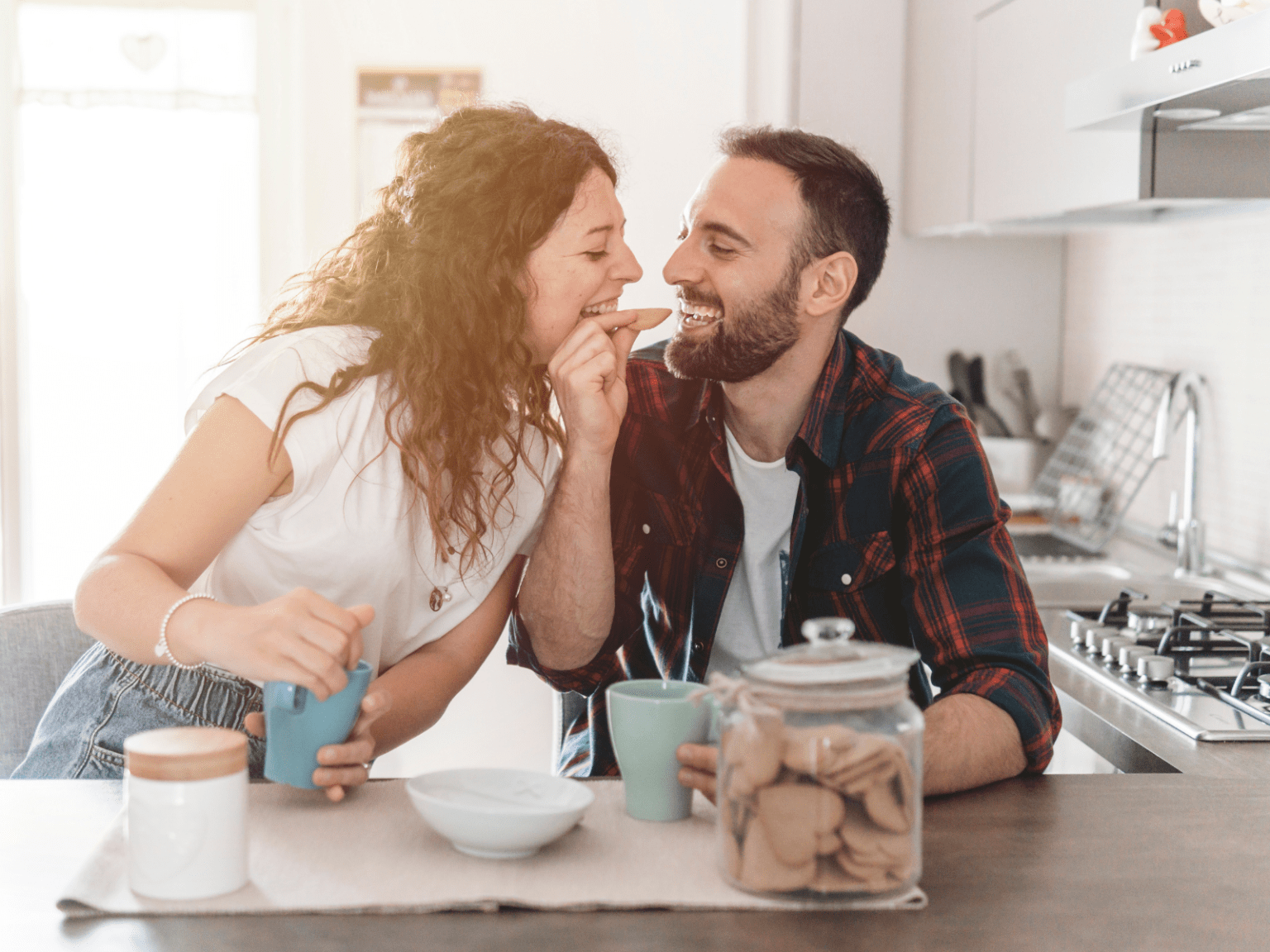 Casal sorridente compartilhando um momento de carinho durante o café da manhã em casa, representando hábitos saudáveis e a rotina do casal no dia a dia.